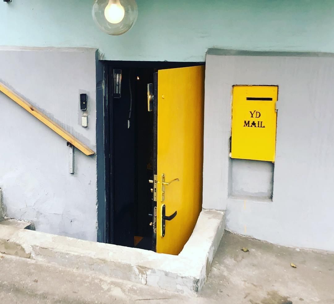 The yellow front door at the bottom of the basement steps, with its own yellow YD MAIL box